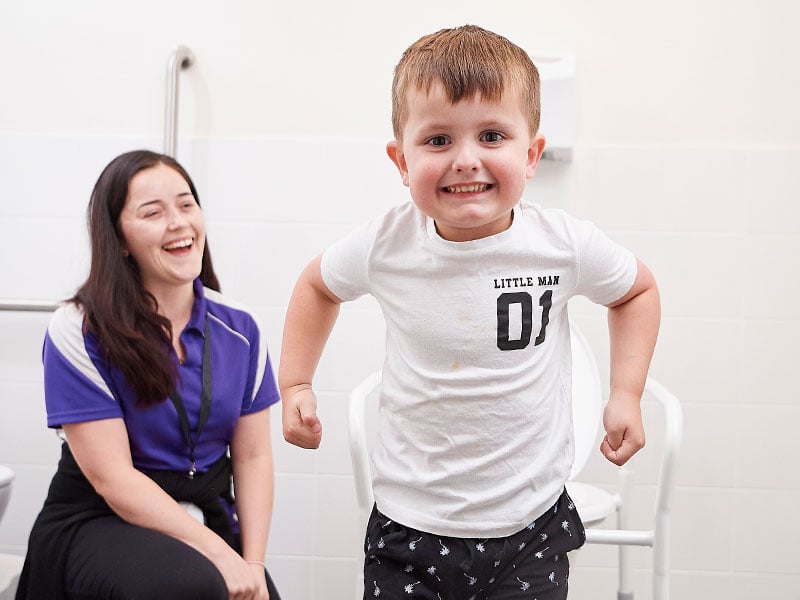 A young boy in a bathroom smiling beside a therapist