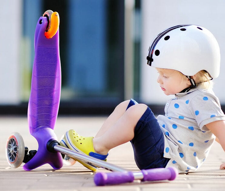 A toddler sitting beside a three wheel scooter