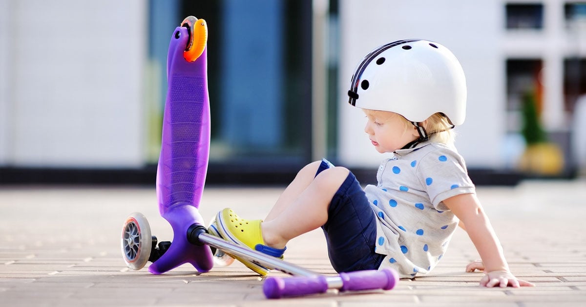 A toddler sitting beside a three wheel scooter
