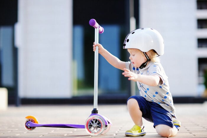 A toddler holding a three wheel scooter