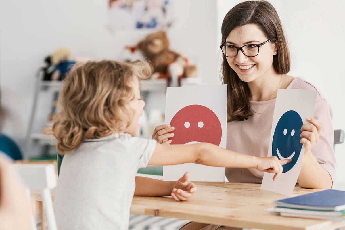 A therapist holding up cards with faces while a young boy points at one