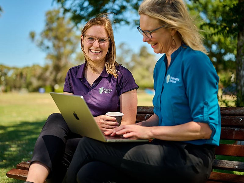 Two smiling therapists sitting on a park bench