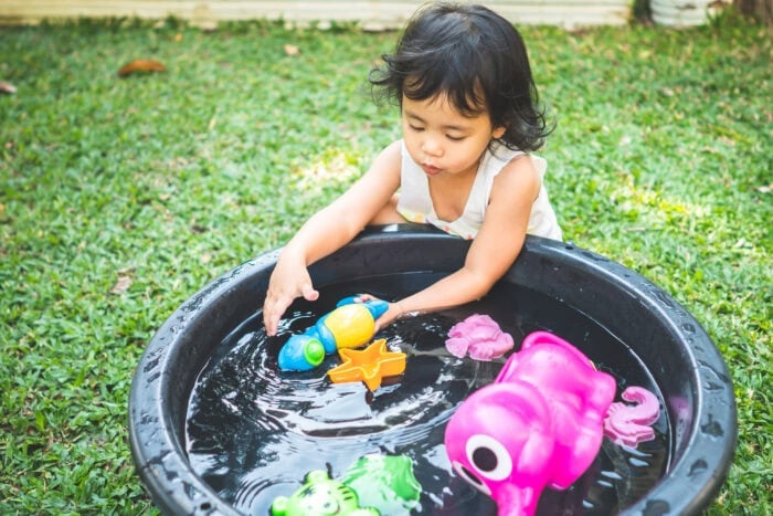 A young girl playing with toys with water in a backyard