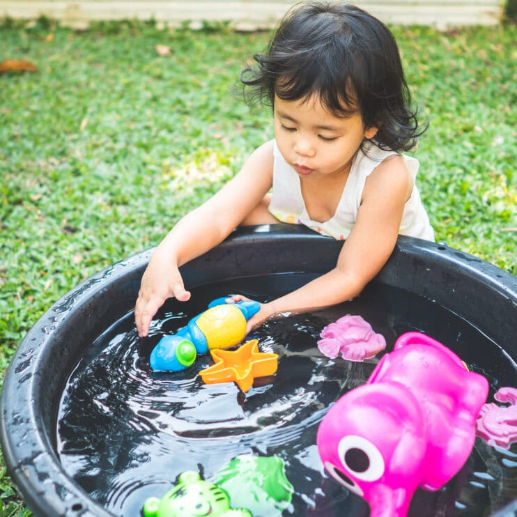 A young girl playing with toys with water in a backyard